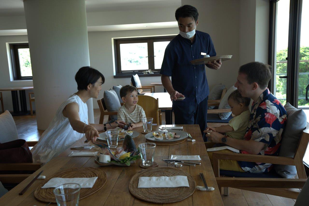 出来上がった料理を運ぶ高田さんと運ばれた料理を興味津々にみるタサン志麻さんファミリー